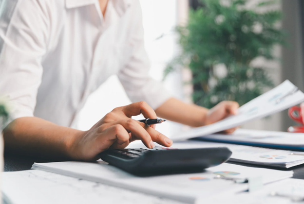 A businesswoman reviewing financial reports and calculating corporation tax payments in an office environment.
