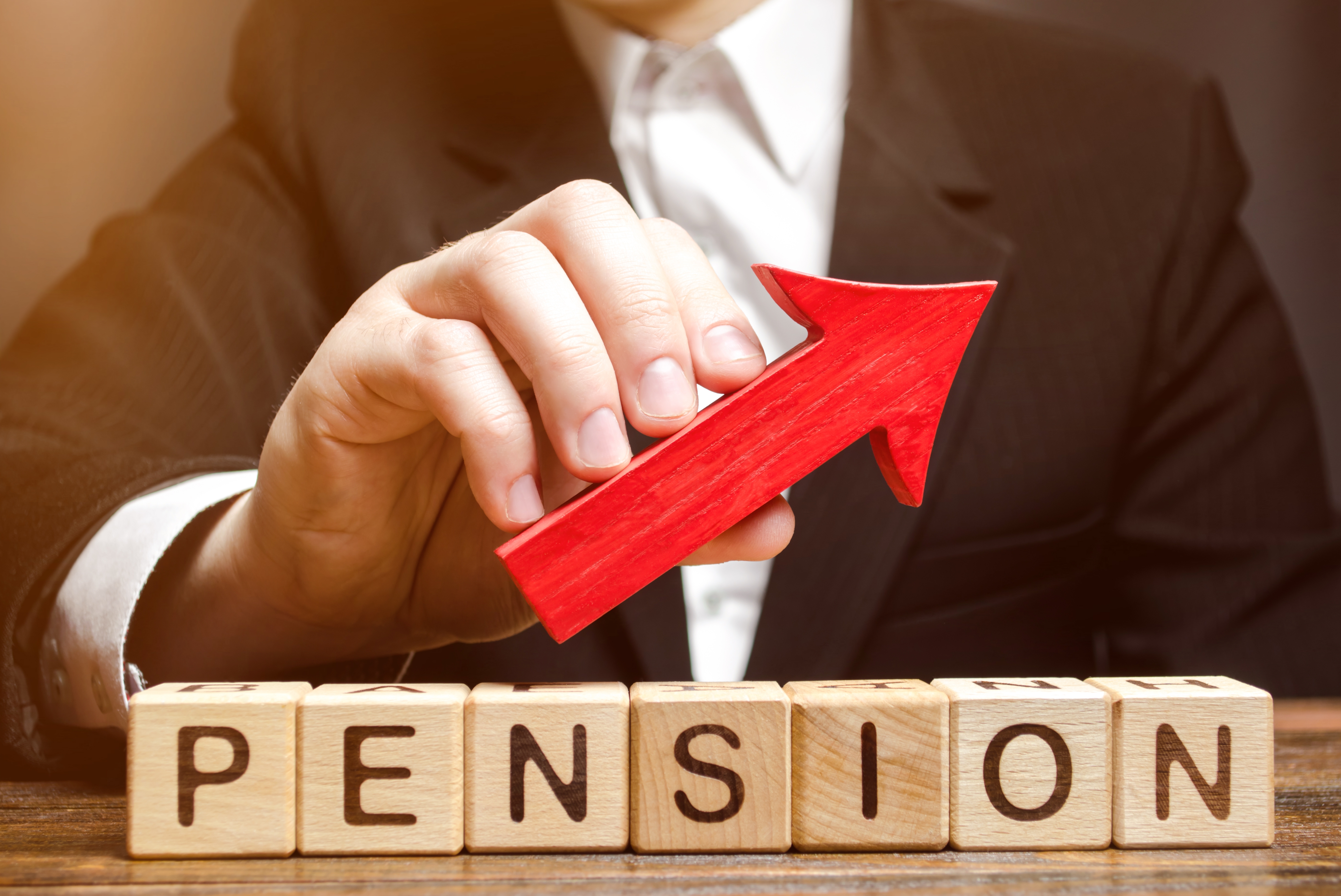 Individual in a suit holding a red arrow pointed up, this is above wooden blocks that read out the word ‘pension’. This image portrays how you can use pension contributions for corporation tax relief.