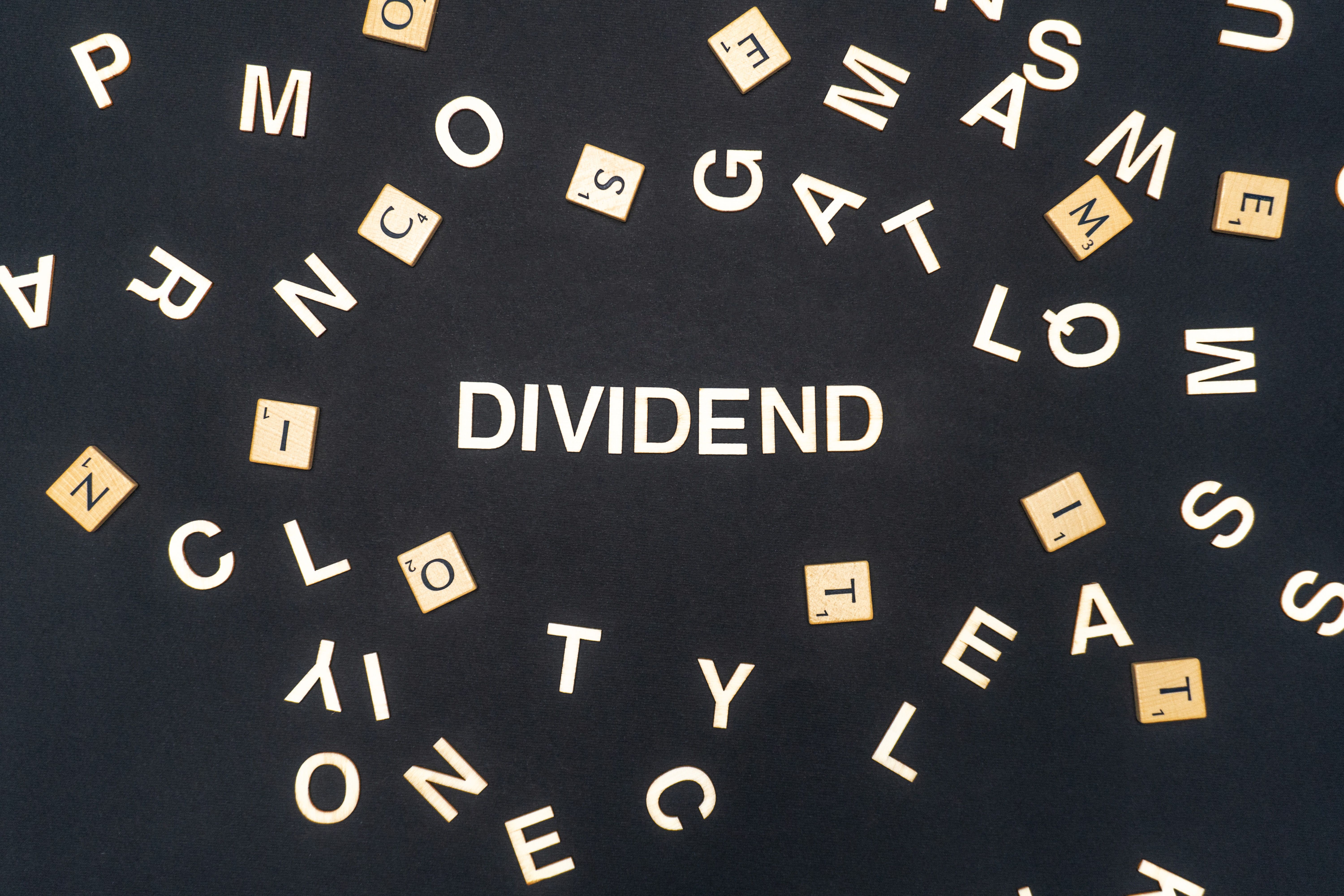 Black background with white letters and beige scrabble pieces scattered around, with the word dividend in the centre.